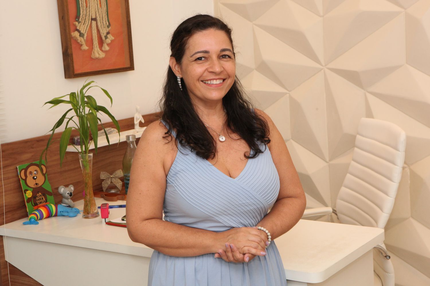 Dra. Letícia em pé no consultório, ao lado da mesa com brinquedos