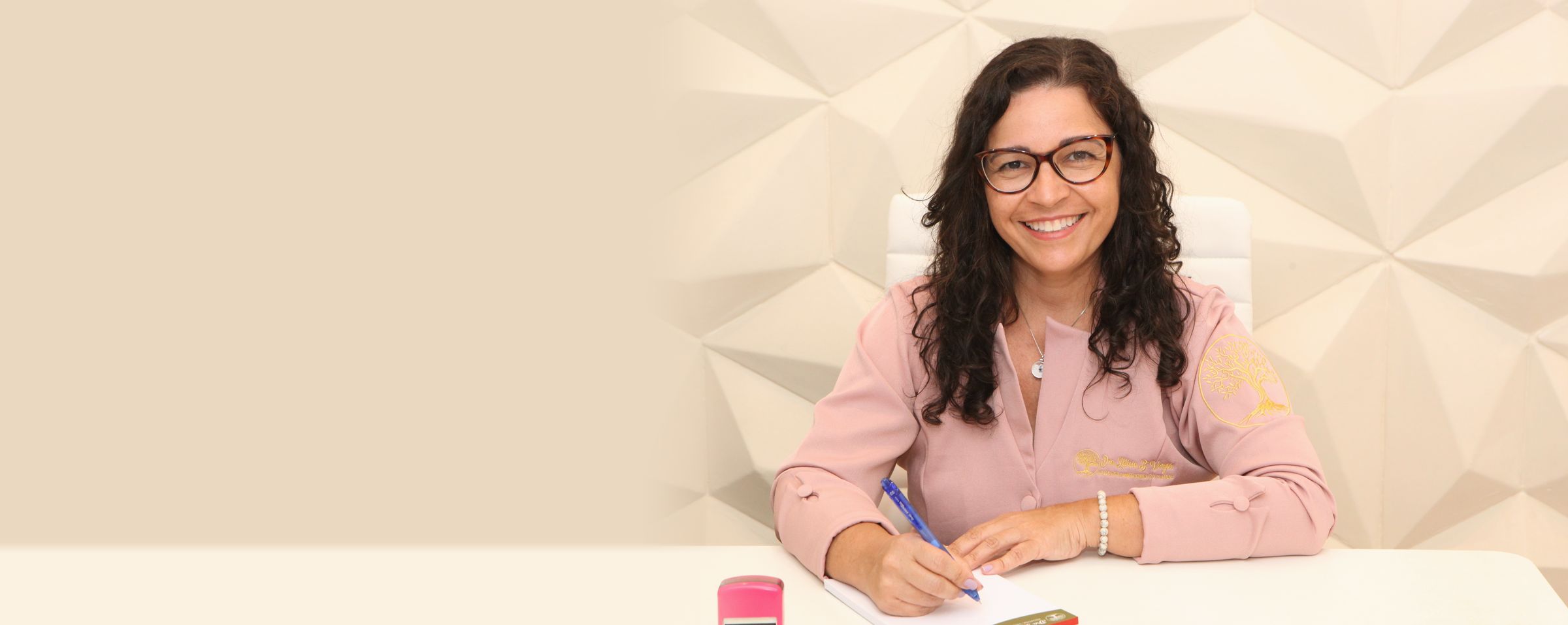 Dra. Letícia Barbosa Vargas, pediatra, sorrindo à mesa do consultório, de jaleco rosa